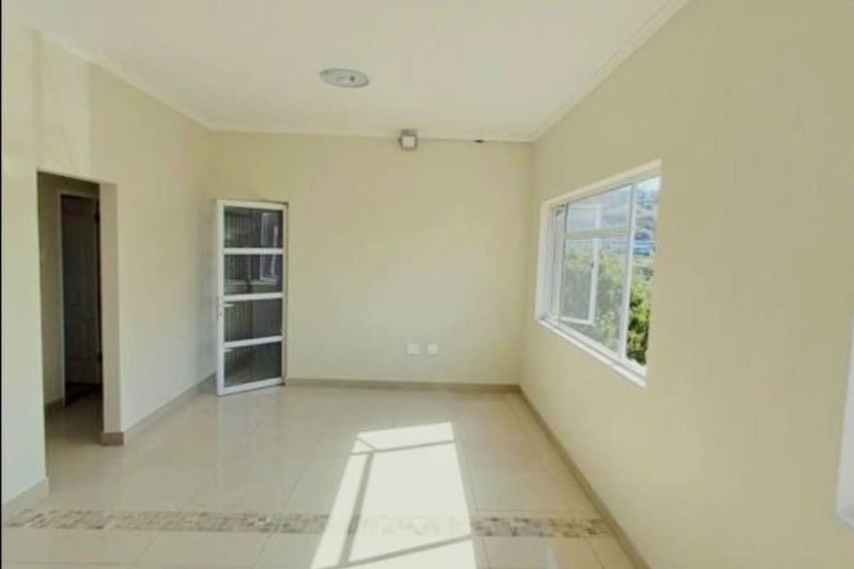 A bright, empty living area featuring neutral tiled flooring, coved ceilings, and large windows providing natural light.