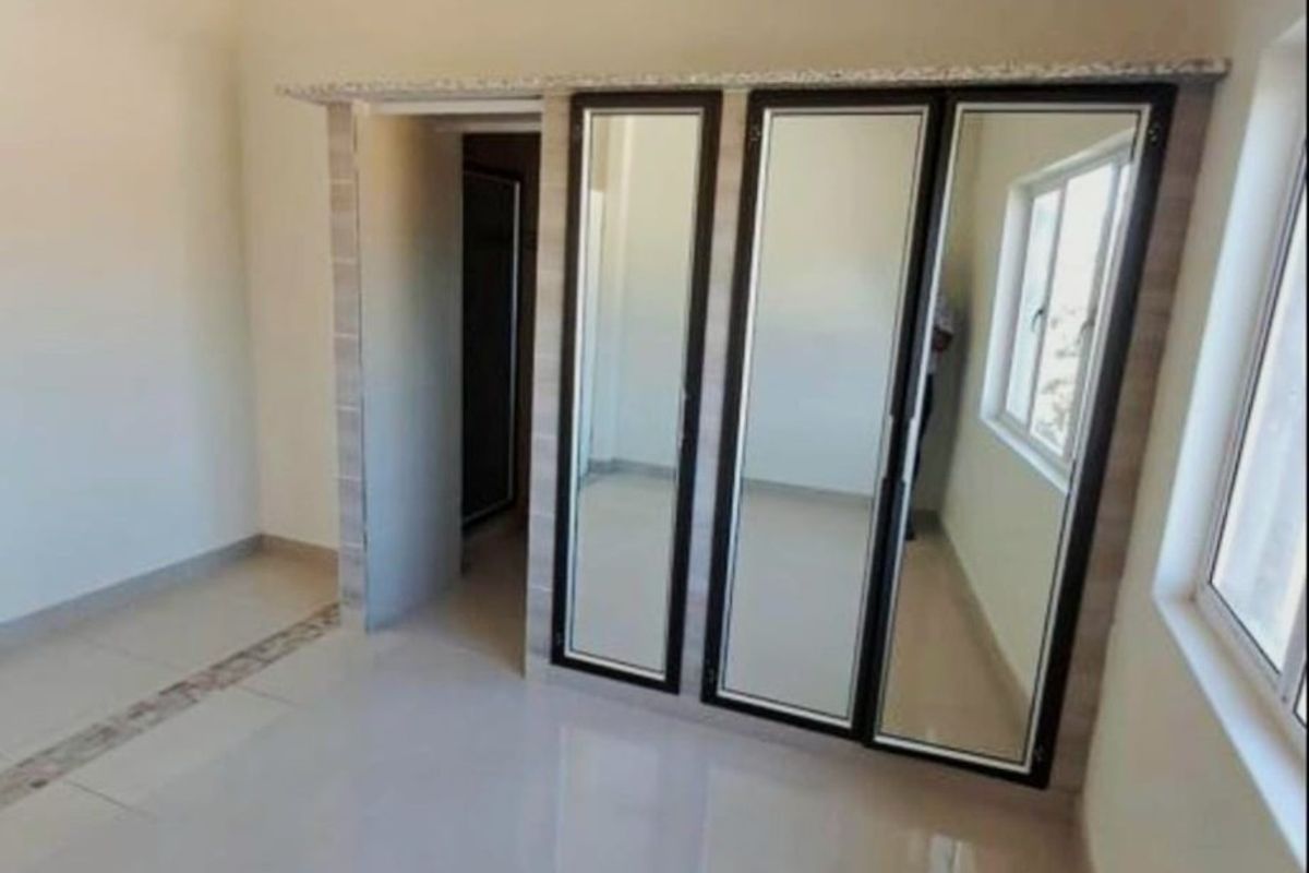 A bright, empty bedroom featuring tiled flooring and a large built-in mirrored wardrobe with dark framing.