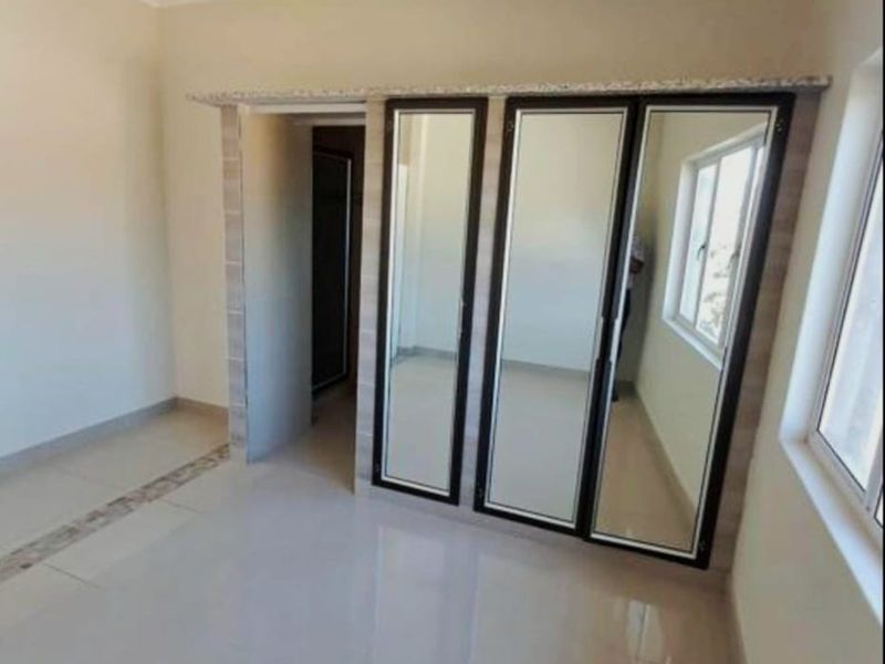 A bright, empty bedroom featuring tiled flooring and a large built-in mirrored wardrobe with dark framing.