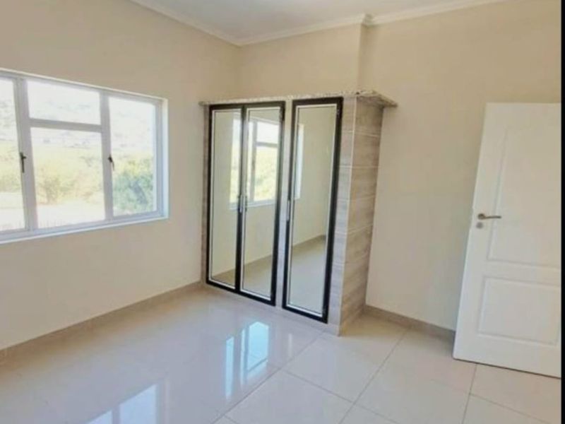A bright, empty bedroom featuring neutral tiled flooring, a built-in wardrobe with mirrored doors, and large windows providing natural light.