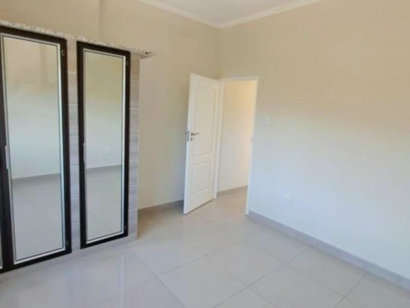 A clean, empty bedroom featuring neutral tiled flooring, built-in cupboards with mirrored doors, and a simple ceiling light fixture.