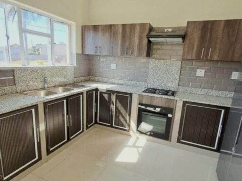 A modern, clean kitchen featuring granite countertops, built-in oven, hob, extractor fan, and ample cabinetry with a tiled splashback.
