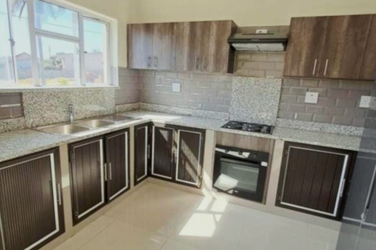 A modern, clean kitchen featuring granite countertops, built-in oven, hob, extractor fan, and ample cabinetry with a tiled splashback.