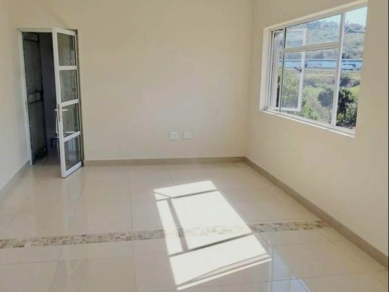A bright, empty living area featuring neutral tiled flooring, a large window with natural light, and a glass panel door leading to an adjacent space.