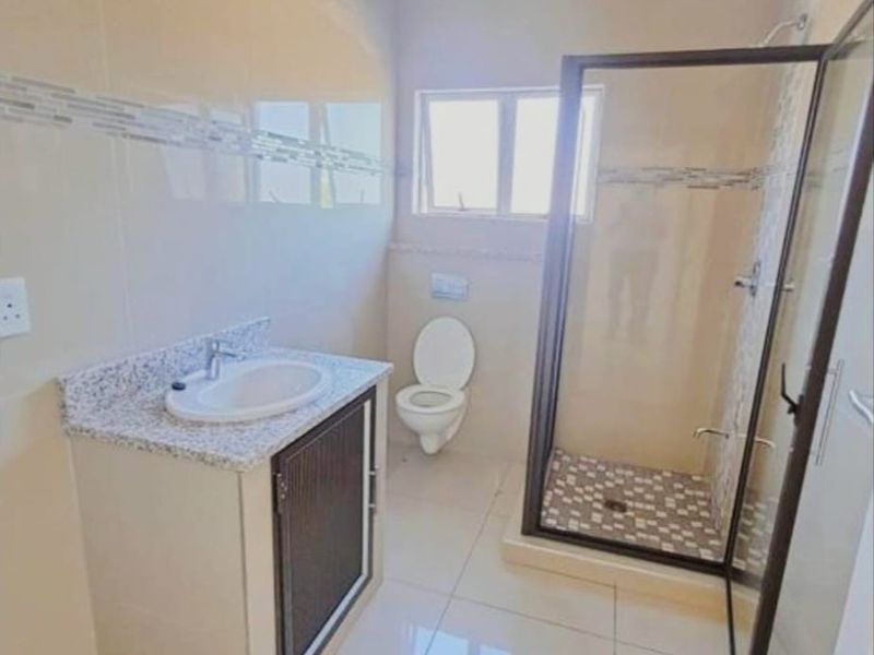 A modern bathroom featuring a vanity with granite countertop, a glass-enclosed shower, and tiled finishes. The space requires final painting and finishing touches.