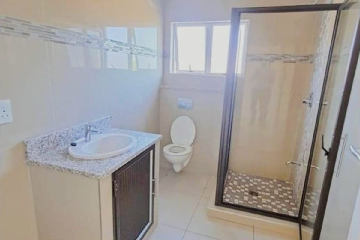 A modern bathroom featuring a vanity with granite countertop, a glass-enclosed shower, and tiled finishes. The space requires final painting and finishing touches.