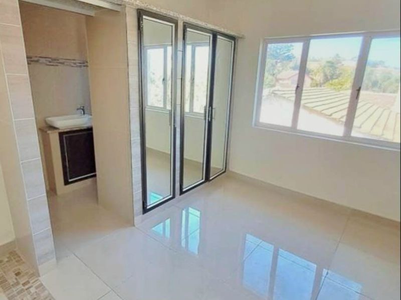 A bright, empty bedroom featuring tiled flooring, built-in mirrored cupboards, and an adjoining en-suite vanity area with large windows.