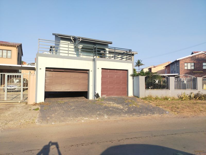 Front exterior view of a double-story house featuring a double garage, paved driveway, and an upper-level balcony with metal railings.