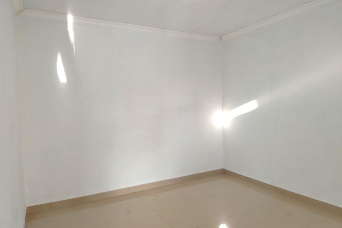 An empty bedroom featuring neutral tiled flooring and simple ceiling cornicing, providing a blank canvas for personalization.