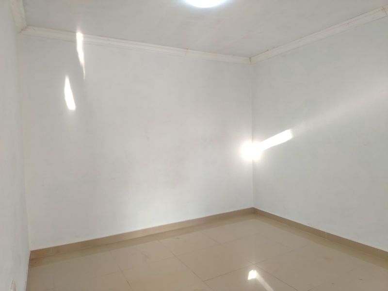 An empty bedroom featuring neutral tiled flooring and simple ceiling cornicing, providing a blank canvas for personalization.