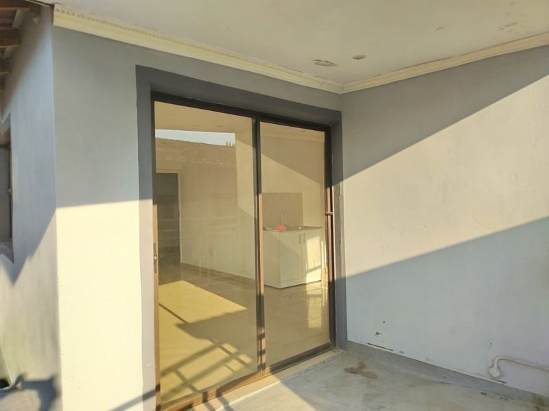 A covered patio area featuring a sliding glass door entrance, tiled flooring, and recessed ceiling lighting, showing some signs of wear on the exterior walls.