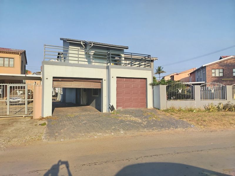 Front elevation of a two-story house featuring a double garage, paved driveway, and an upper-level balcony with metal railings.