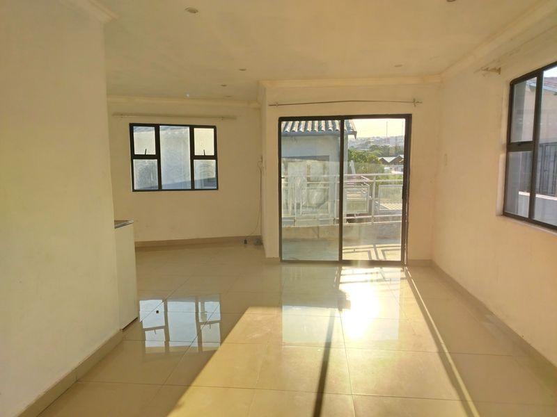 An empty open-plan living area featuring polished floor tiles, recessed lighting, and a sliding glass door leading to an outdoor space.
