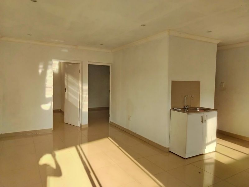 An open-plan living area featuring tiled flooring, recessed lighting, and a compact kitchenette with built-in cabinetry and a sink.
