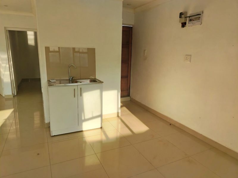 A compact, empty kitchen area featuring a single stainless steel sink unit, tiled flooring, and neutral wall finishes.