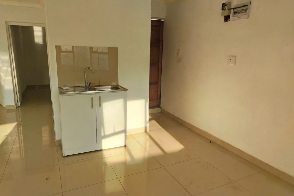 A compact, empty kitchen area featuring a single stainless steel sink unit, tiled flooring, and neutral wall finishes.