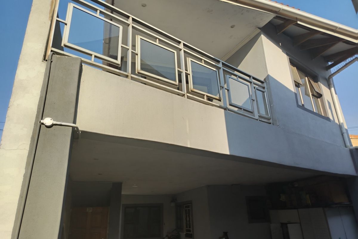 Rear elevation of the property featuring a balcony with a metal and glass balustrade, recessed lighting, and a tiled roof structure.