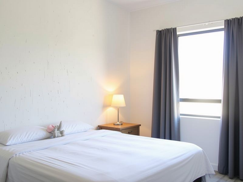 A simple bedroom featuring a textured accent wall and a window with grey curtains, providing a neutral and functional sleeping space.