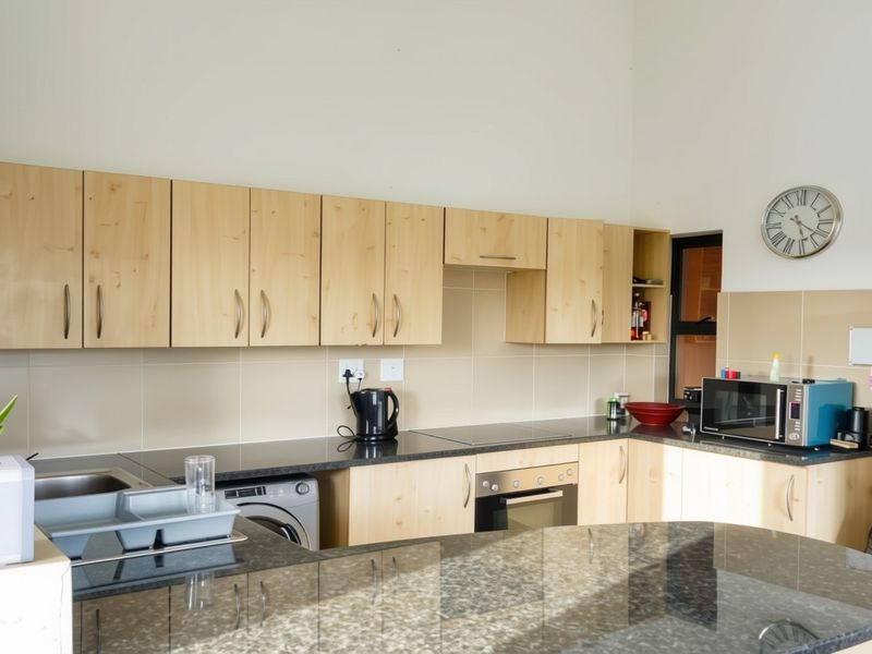 A functional kitchen featuring light wood cabinetry, granite countertops, a built-in oven, electric hob, and an integrated washing machine.