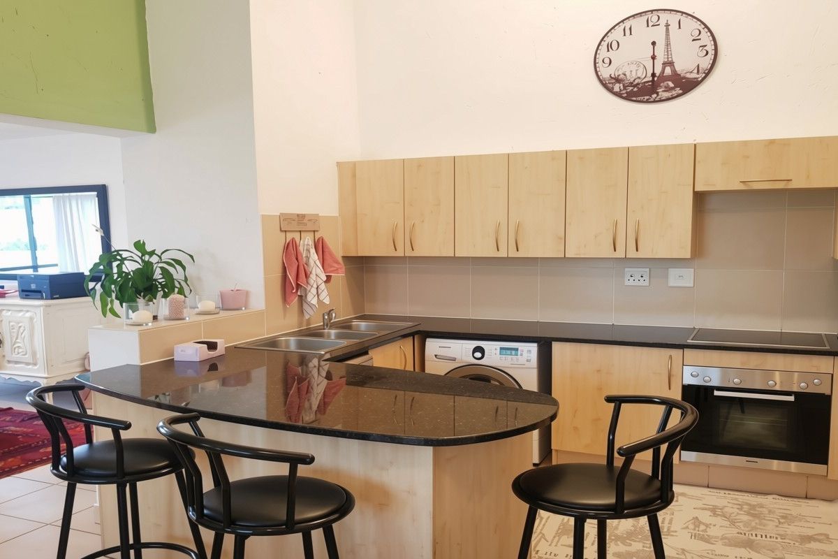 A functional kitchen featuring light wood cabinetry, dark granite countertops, a built-in oven, hob, and an integrated washing machine with a breakfast bar area.