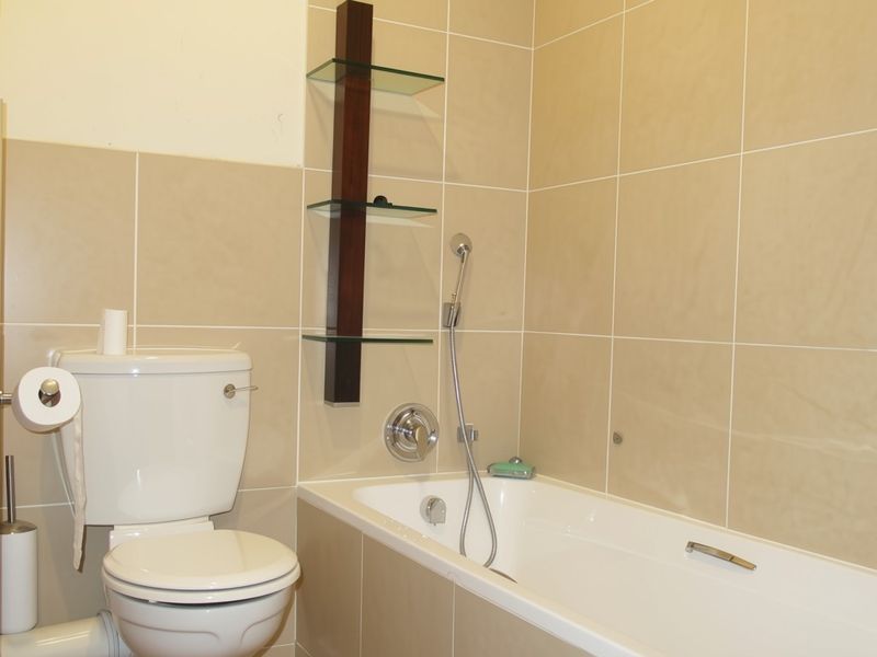 A functional bathroom featuring a bathtub with a handheld shower attachment, a standard toilet, and neutral ceramic wall tiling.