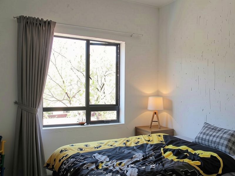 A bedroom featuring a window with aluminium frames and curtain rails, showing some wear on the wall surfaces.