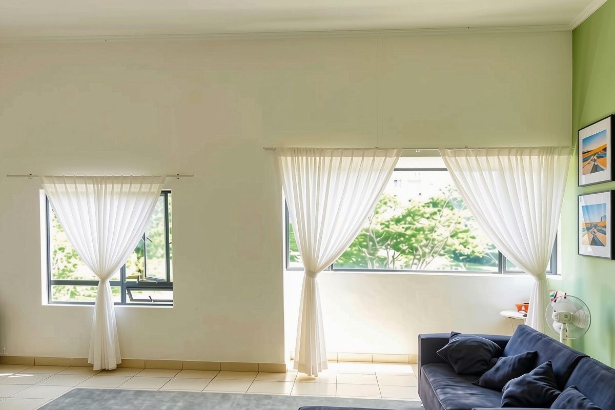A bright living room featuring tiled flooring, large windows with sheer curtains, and a green accent wall, providing a clean and well-maintained living space.