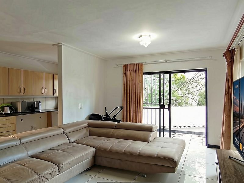 Open-plan living area featuring a modern kitchen with built-in cabinetry and appliances, flowing seamlessly to a private balcony through sliding glass doors.