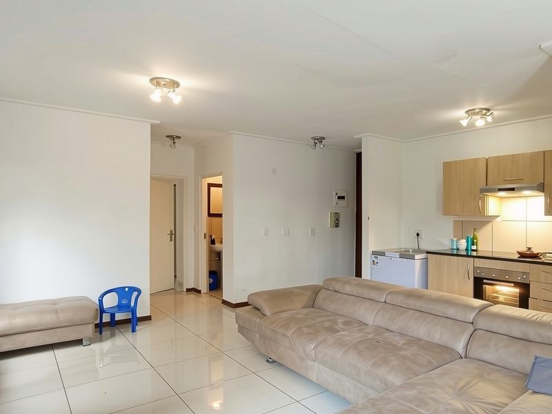 Open-plan living area featuring tiled flooring, integrated kitchen cabinetry with built-in oven and extractor fan, and recessed spotlighting throughout the space.