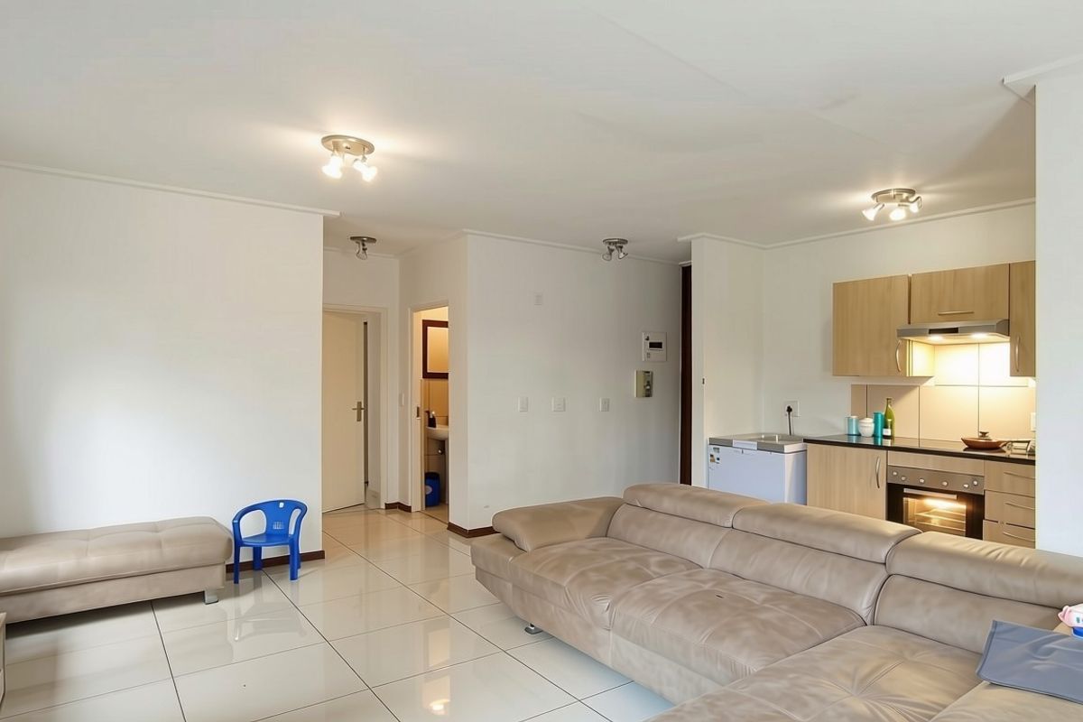 Open-plan living area featuring tiled flooring, integrated kitchen cabinetry with built-in oven and extractor fan, and recessed spotlighting throughout the space.