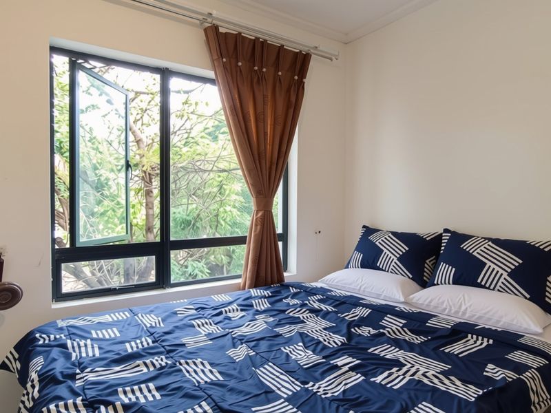 A functional bedroom featuring a large casement window that provides natural light and views of the surrounding greenery.