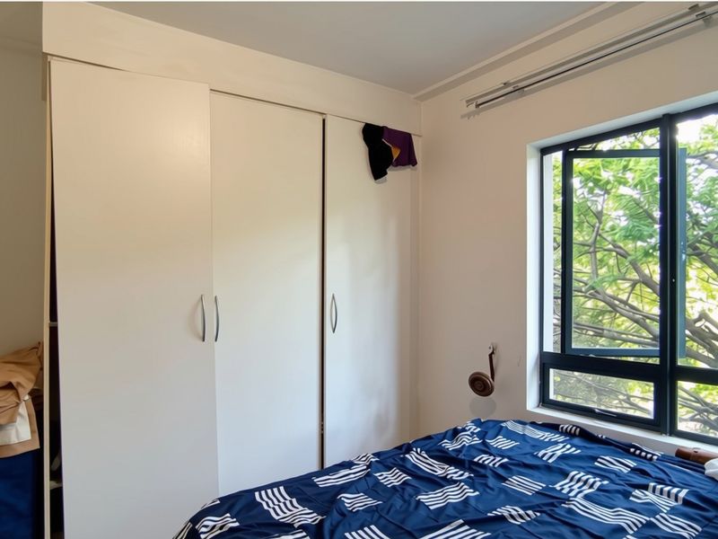 A bedroom featuring a built-in wardrobe and a large window with an aluminium frame, providing natural light and a view of greenery.