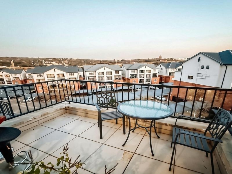 A spacious balcony featuring tiled flooring and a metal balustrade, offering elevated views of the surrounding apartment complex.