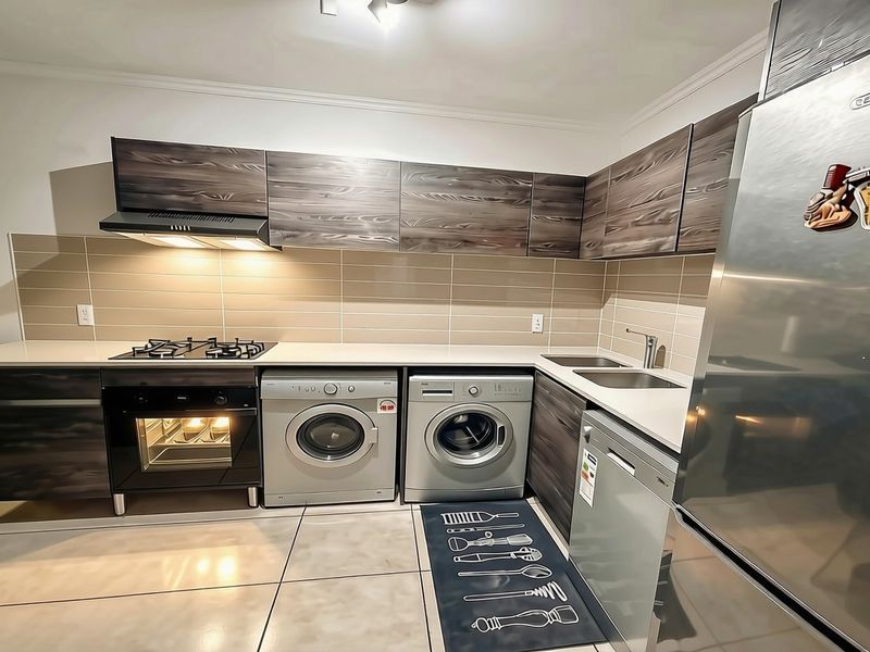 Modern kitchen featuring dark wood-grain cabinetry, stone countertops, integrated gas hob, oven, extractor fan, and dedicated space for laundry appliances.