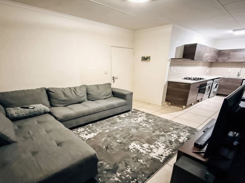 Open-plan living area featuring a modern kitchen with built-in cabinetry, gas hob, and tiled flooring, seamlessly connected to the lounge space.