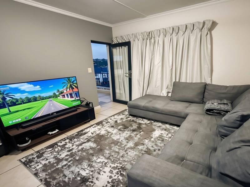 A comfortable living room featuring tiled flooring, crown molding, and direct access to an outdoor balcony through a glass sliding door.