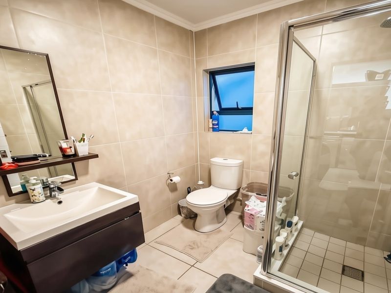 A functional bathroom featuring a modern vanity cabinet, a glass-enclosed shower, and neutral wall tiling throughout.