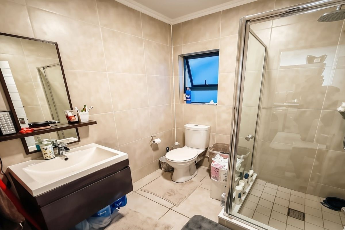 A functional bathroom featuring a modern vanity cabinet, a glass-enclosed shower, and neutral wall tiling throughout.