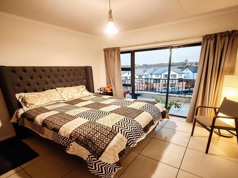 A well-lit bedroom featuring tiled flooring and a large sliding glass door that provides direct access to a private balcony.
