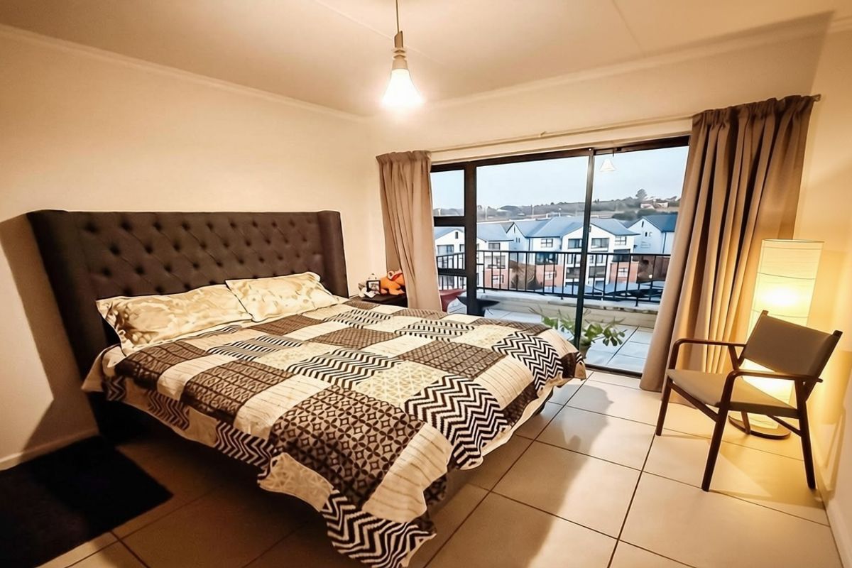 A well-lit bedroom featuring tiled flooring and a large sliding glass door that provides direct access to a private balcony.