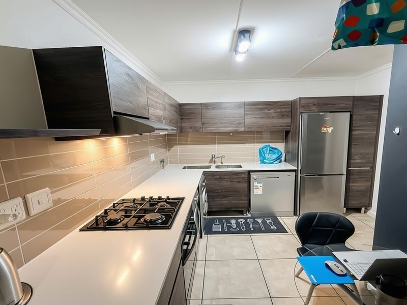 Modern kitchen featuring dark wood-grain cabinetry, a gas hob with extractor fan, tiled backsplash, and ample counter space.