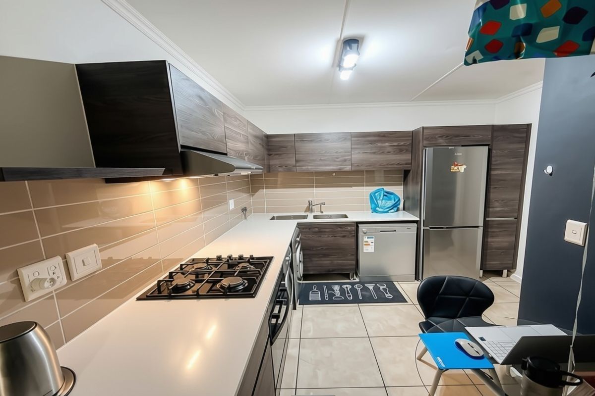 Modern kitchen featuring dark wood-grain cabinetry, a gas hob with extractor fan, tiled backsplash, and ample counter space.