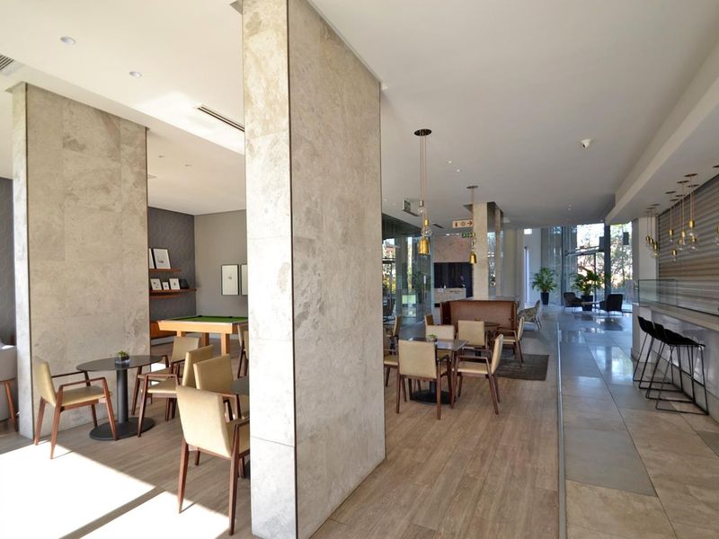 Modern clubhouse area featuring stone-clad columns, a built-in bar counter, and a mix of tiled and wood-look flooring in a well-maintained communal space.