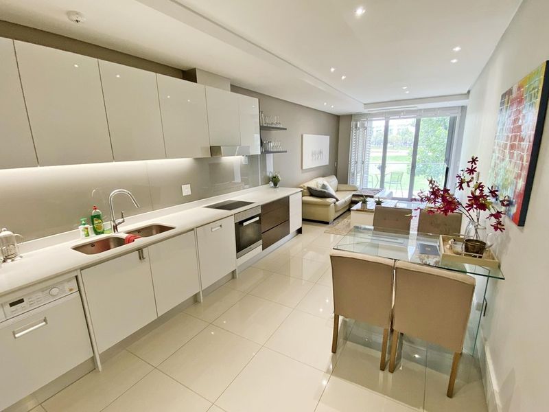 Modern open-plan living area featuring a sleek kitchen with high-gloss cabinetry, stone countertops, integrated appliances, and seamless flow to a private balcony.