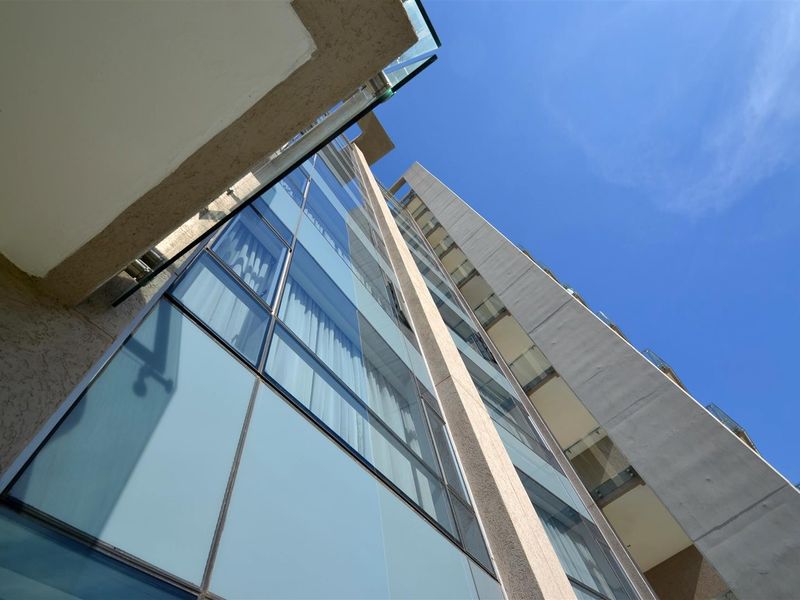 Low angle view of a modern apartment building facade featuring extensive glass curtain walling and concrete structural elements.