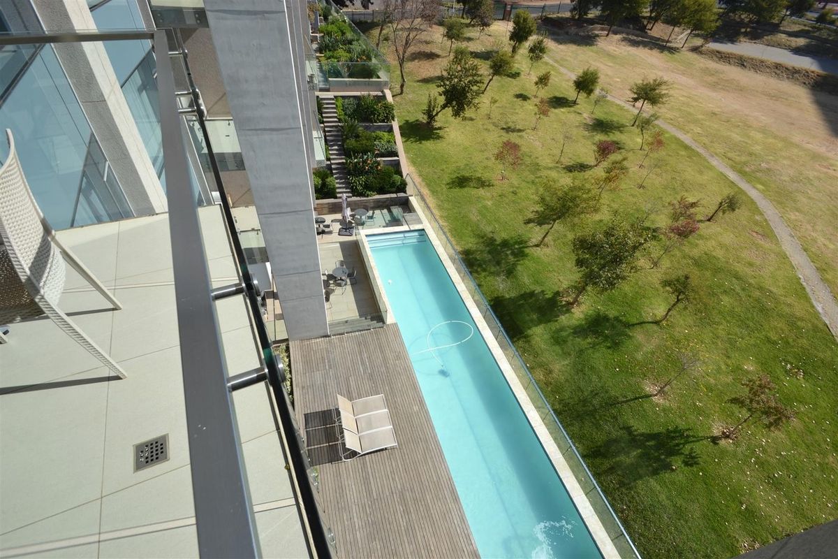 Elevated view from a balcony overlooking a modern swimming pool, timber deck, and landscaped communal garden area.
