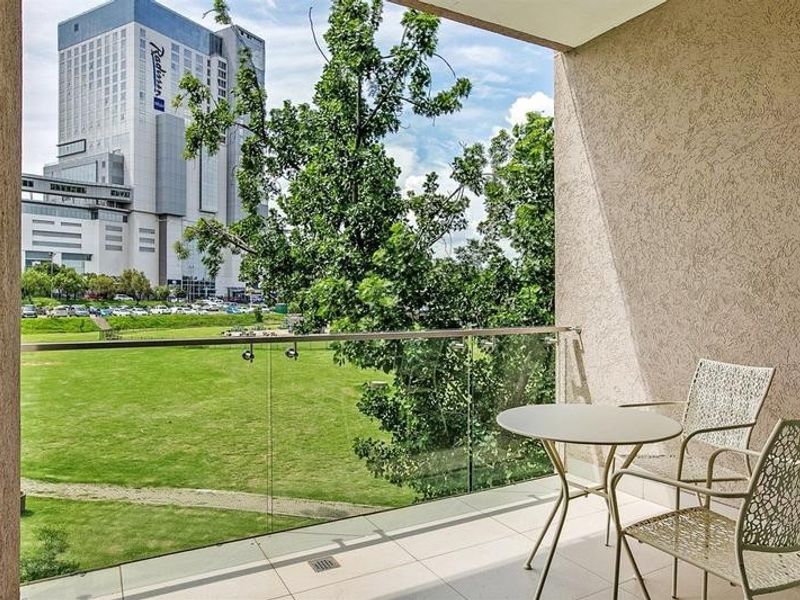 A covered balcony featuring a modern glass balustrade with stainless steel railings, tiled flooring, and an open outlook over a green space.