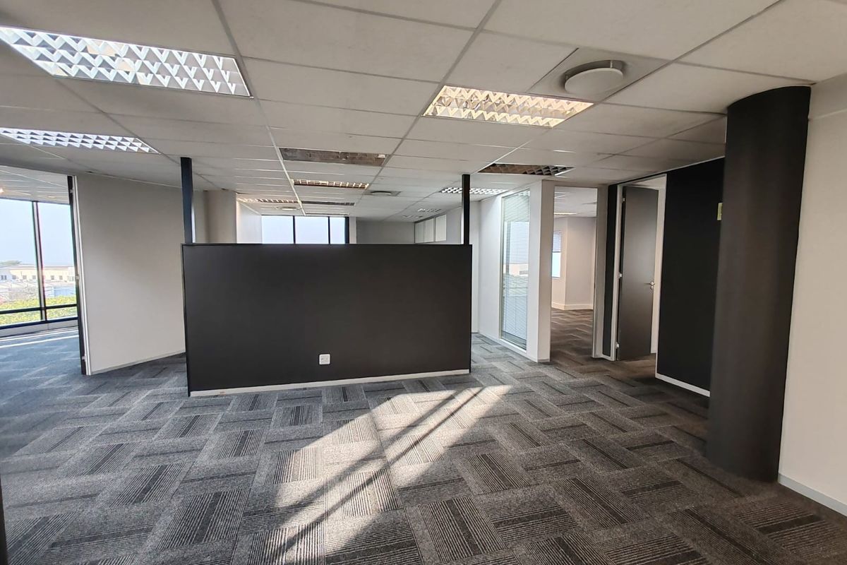 An open-plan office space featuring carpet tiles, a suspended ceiling with recessed lighting, and a central partition wall.