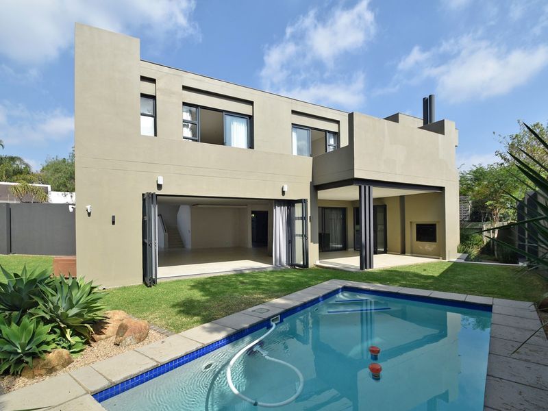 Modern double-story rear elevation featuring a swimming pool, covered patio with built-in fireplace, and large stacking doors opening to the living area.