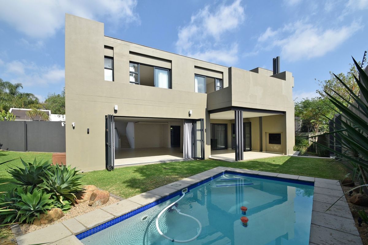 Modern double-story rear elevation featuring a swimming pool, covered patio with built-in fireplace, and large stacking doors opening to the living area.